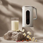 White AmonNusy Nut Milk Maker frother on a stone block with a glass of milk and flowers on a neutral background