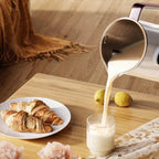 Café au lait being poured into a glass on a wooden table with croissants and lemons.