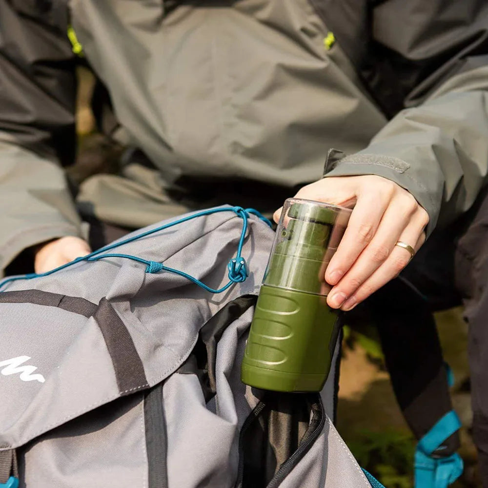 Person holding a green mug next to a gray bag outdoors