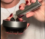 Person using a Avinora 3 in 1 Hair Growth Scalp Massager with a black and red design, applying a clear gel-like substance from a bottle.