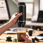 Hand using a CofeMeki Portable Coffee Maker to pour coffee into a glass on a desk.