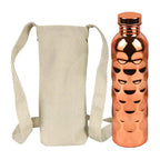 A CopperSyp Copper Water Bottle with a honeycomb pattern and a metallic cap, shown next to a beige canvas sleeve with shoulder straps on a white background.