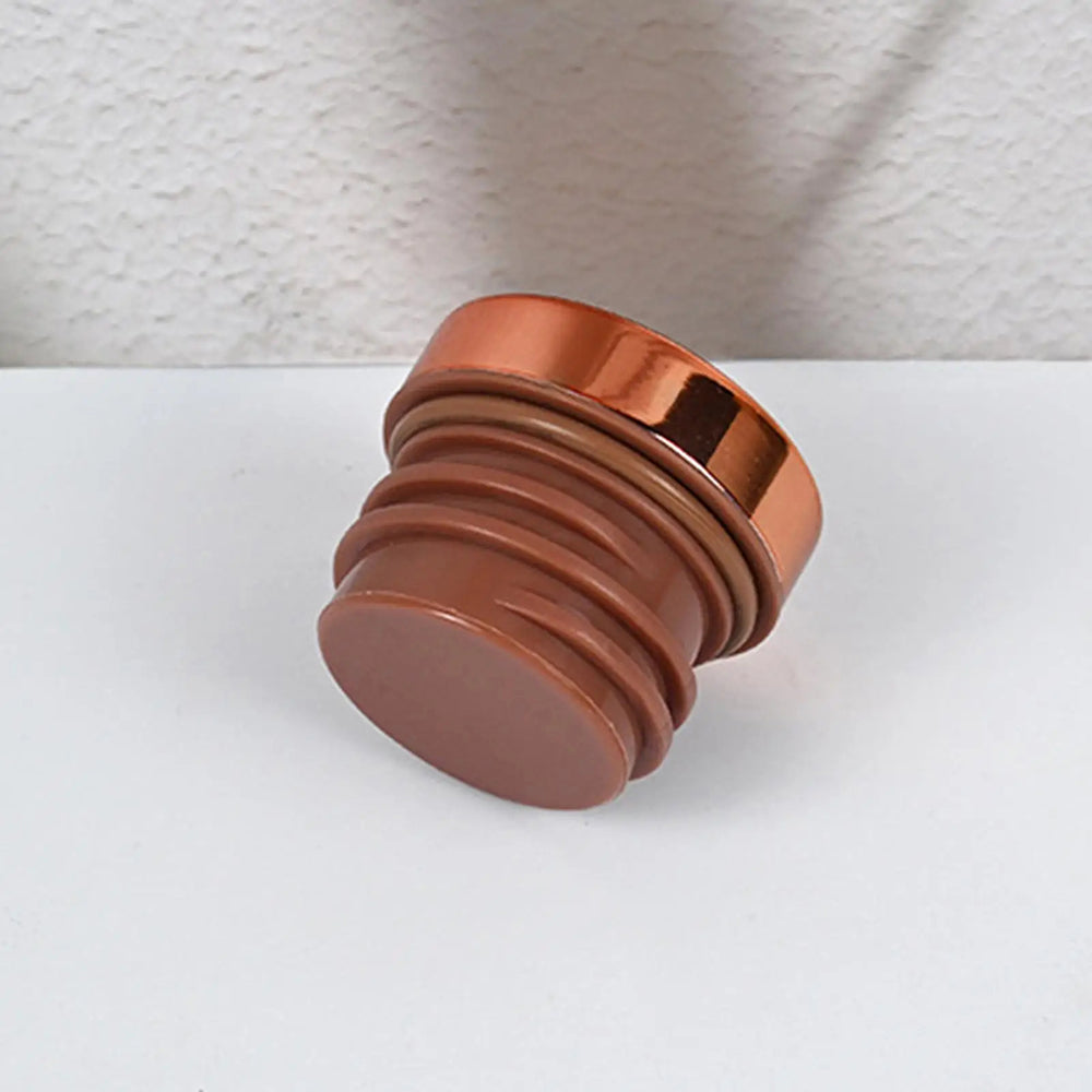 A metallic copper-colored cylindrical knob or decorative hardware piece with a ribbed base, shown on a white surface against a textured white wall.