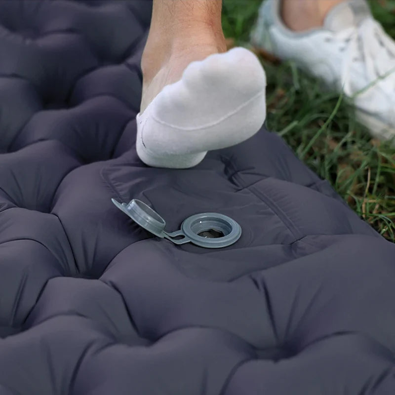 Person using a blue inflatable DuoRestor Pro Camping Mattress outdoors with grass visible.