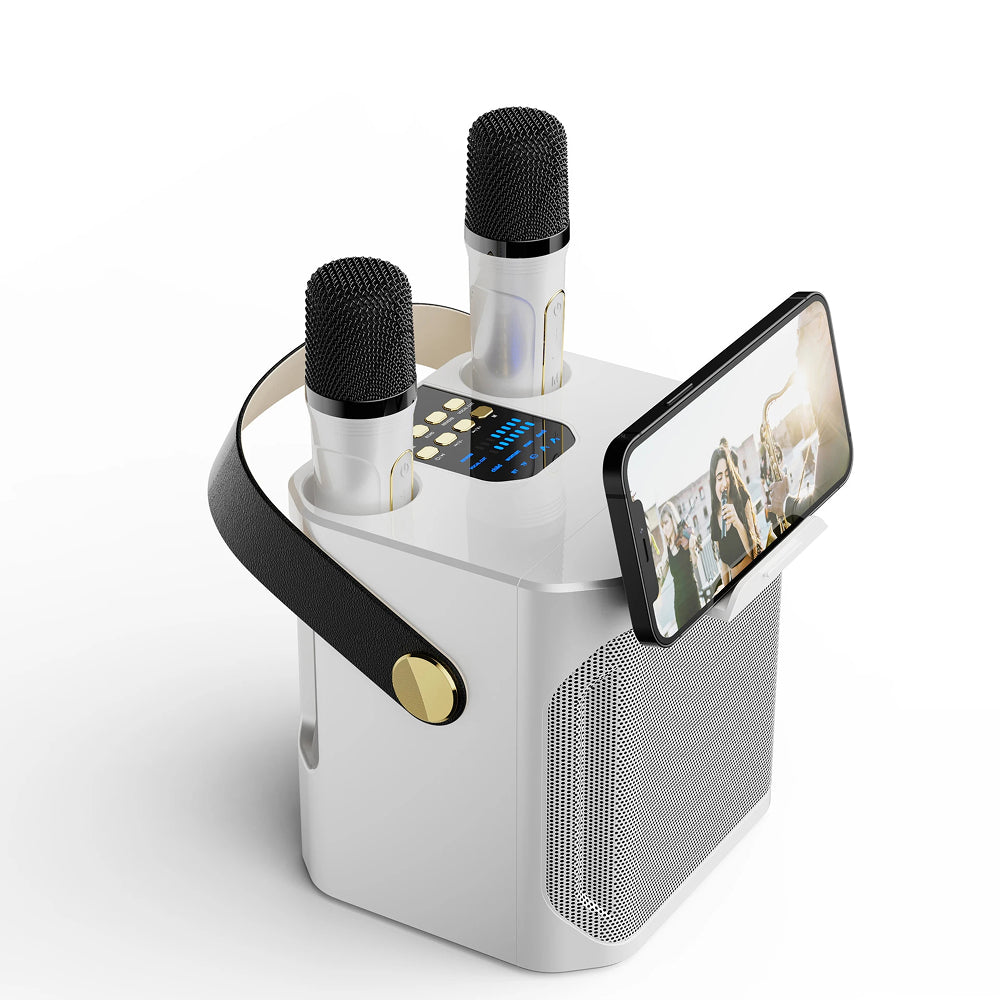 A white portable FolbGent Karaoke Machine with two built-in microphones, a black carrying handle with a gold button, and a built-in phone holder displaying a video call.