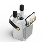 A white portable FolbGent Karaoke Machine with two built-in microphones, a black carrying handle with a gold button, and a built-in phone holder displaying a video call.