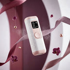 White and pink Gloreine IPL Hair Removal Device with digital display on a purple background with ribbons and flowers.