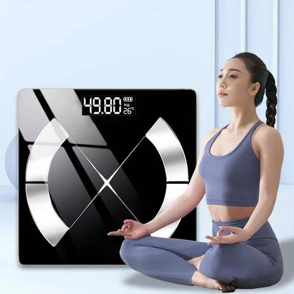 A woman in a blue-gray sports bra and leggings sits cross-legged beside a large MillKindy Smart Body Scale. The scale has a black face with reflective silver geometric accents and a digital readout showing 49.
