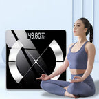 A woman in a blue-gray sports bra and leggings sits cross-legged beside a large MillKindy Smart Body Scale. The scale has a black face with reflective silver geometric accents and a digital readout showing 49.