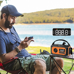 Man sitting by a lake using a smartphone with an orange and black portable Tiverno Emergency Radio on a table next to him.