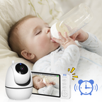 Baby lying on a bed drinking from a bottle with a Wavel Baby Monitor displaying the video feed.