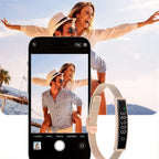 A Zylos Smart Fitness Bracelet with a beige mesh band and a black digital display is shown in front of a smartphone screen displaying a photo of a couple, with a real couple also pictured in the background.