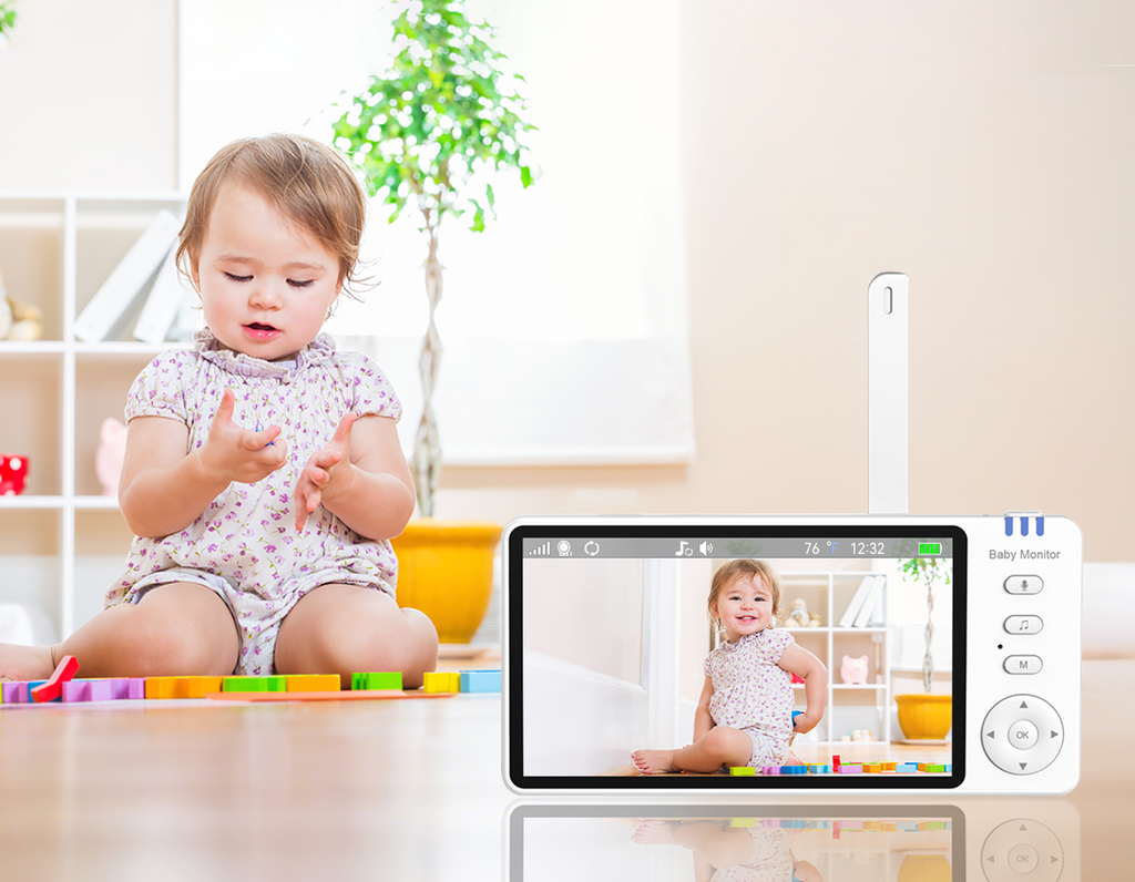 Baby sitting on the floor with a Wavel Baby Monitor displaying a video of itself, in a room with a plant and shelves.
